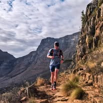 Trail runner on a rocky mountain path above Cape Town with sandstone cliffs and valley behind