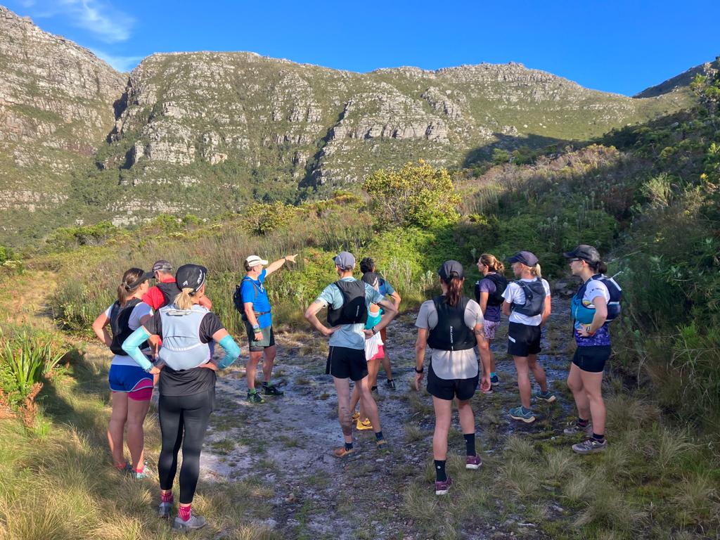 A guide briefing a group of trail runners on a rocky mountain path above Cape Town before a supported challenge
